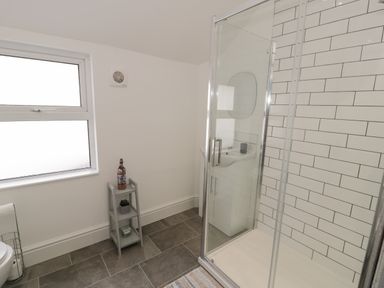 A bathroom with a glass shower enclosure white tiled wall a small shelving unit and frosted window at Bryn Derfel in Borth-y-Gest near Porthmadog