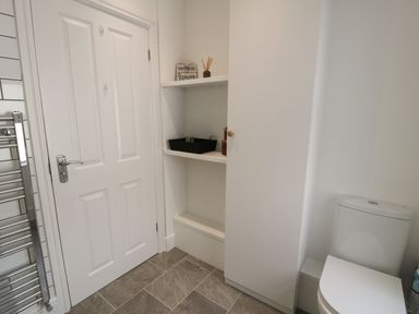 A bathroom with a white door a white storage cabinet open shelves with items and a white toilet at Bryn Derfel in Borth-y-Gest near Porthmadog
