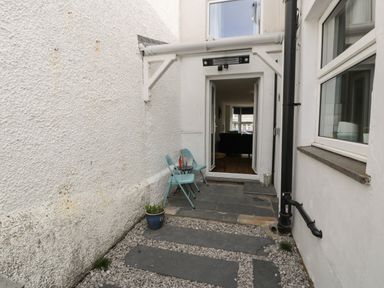 A small outdoor patio area with two blue chairs and a small table near an open door at Bryn Derfel in Borth-y-Gest near Porthmadog