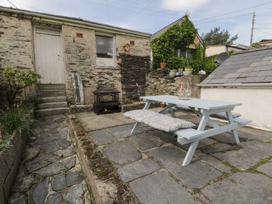 An outdoor patio area with a picnic table and cushions next to a stone building with a door and window at Bryn Derfel in Borth-y-Gest near Porthmadog