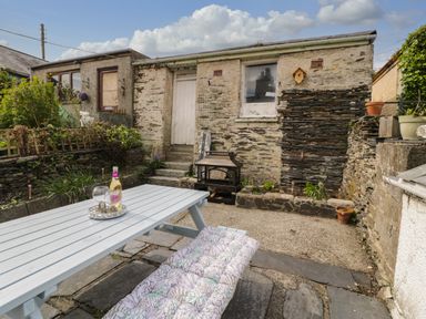 A backyard with a white picnic table and bench cushion near stone walls and a stone building at Bryn Derfel in Borth-y-Gest near Porthmadog