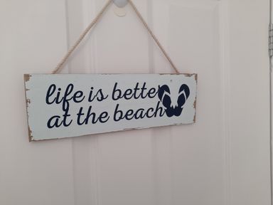 A wall hanging sign with the text life is better at the beach and an image of flip flops