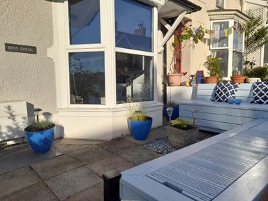 A patio area with blue flower pots and white wooden outdoor furniture at Bryn Derfel in Borth-y-Gest near Porthmadog
