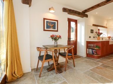 A kitchen dining area with a wooden table two chairs flowers on the table and a wooden door at The Little Hay Barn in Bacton