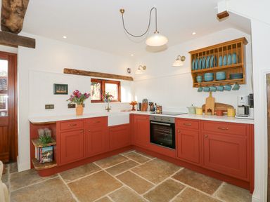 A kitchen with red cabinets and stone tile floor at The Little Hay Barn in Bacton