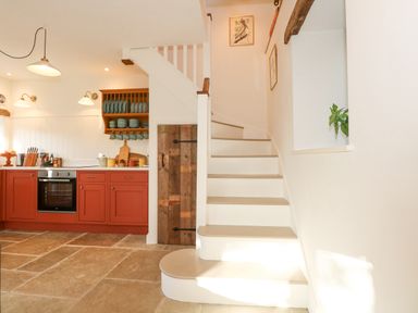 A kitchen with red cabinets and a staircase with wooden door underneath at The Little Hay Barn in Bacton