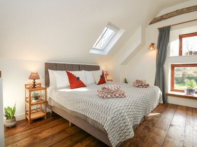 A bedroom with a bed two bedside tables with lamps a skylight window and wooden floors at The Little Hay Barn in Bacton