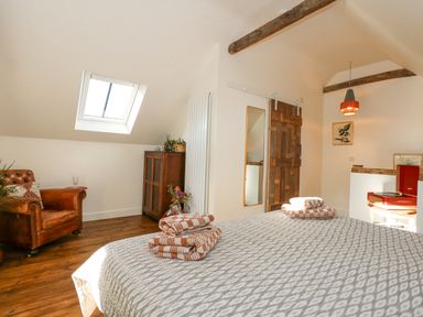 A bedroom with a bed with folded towels a brown leather armchair a wooden cabinet and a barn door at The Little Hay Barn in Bacton