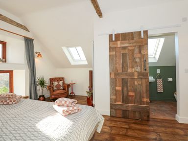 A bedroom with a bed folded towels armchair and a wooden sliding door leading to a bathroom at The Little Hay Barn in Bacton