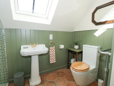 A bathroom with a white pedestal sink wooden toilet seat green panel walls and a small table at The Little Hay Barn in Bacton