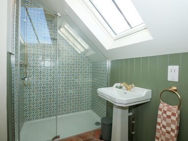 A bathroom with a walk-in shower with patterned tiles a white pedestal sink and skylight at The Little Hay Barn in Bacton
