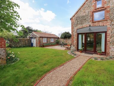 A garden with a gravel path leading to a stone building with glass doors and an outdoor seating area at The Little Hay Barn in Bacton