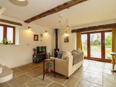 A living room with a fireplace television sofa and wooden beams at The Little Hay Barn in Bacton