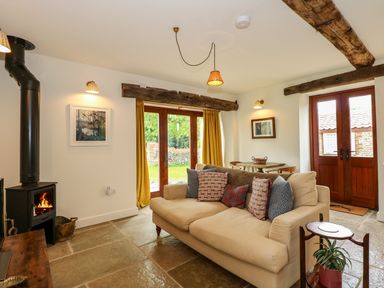 A living room with a beige sofa cushions wood burning stove and wooden doors at The Little Hay Barn in Bacton