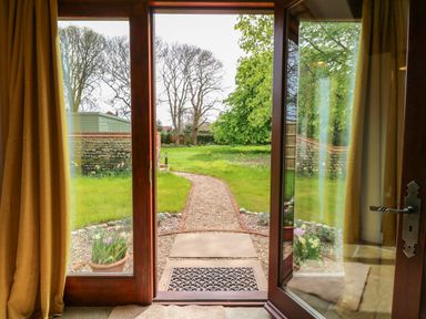 A doorway with glass doors opening to a garden with a gravel path and grassy area at The Little Hay Barn in Bacton
