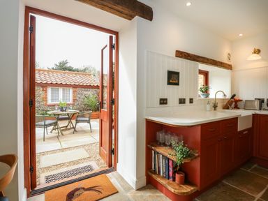A kitchen with red cabinets and a view of an outdoor patio with a table and chairs at The Little Hay Barn in Bacton