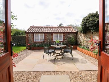 A patio area with a round table and two chairs surrounded by gravel and garden beds at The Little Hay Barn in Bacton