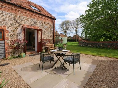 An outdoor patio area with a small round dining table and two chairs beside a stone and brick building at The Little Hay Barn in Bacton