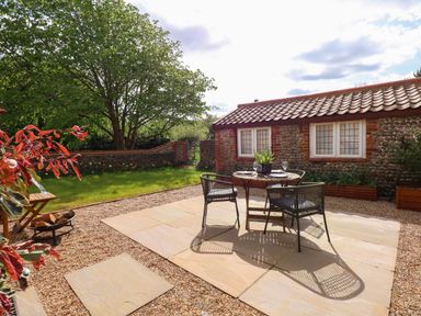 A patio with a table and chairs next to a stone cottage and garden at The Little Hay Barn in Bacton