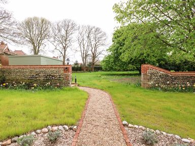A garden path with stone edging between grassy areas and stone walls with flowers at The Little Hay Barn in Bacton