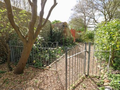 A garden with a gravel path metal gates plants and stone walls at The Little Hay Barn in Bacton