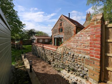An outdoor pathway beside a stone and brick house with a small outbuilding and garden area at The Little Hay Barn in Bacton