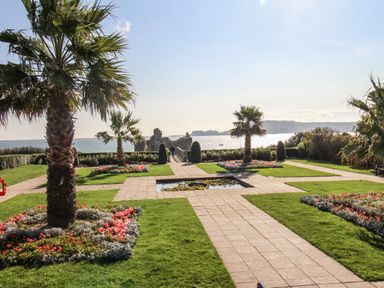 A garden with palm trees flower beds and a central water feature overlooking the sea at Castle Cove View in Castle Cove