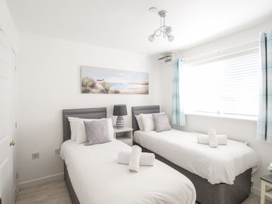 A bedroom with two single beds a nightstand with a lamp a window with blinds and curtains and a beach painting on the wall at Castle Cove View in Castle Cove