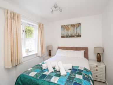A bedroom with a double bed with white linens and a blue patterned blanket with towels on it and two bedside tables with lamps at Castle Cove View in Castle Cove