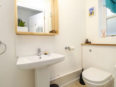 A bathroom with a white sink and toilet a wooden framed mirror and a window with a blue towel at Castle Cove View in Castle Cove