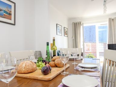 A dining table set with plates glasses and bread in a room with framed pictures and a large window at Castle Cove View in Castle Cove