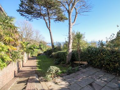 A garden with trees a paved walkway and a tiled patio overlooking water at Castle Cove View in Castle Cove