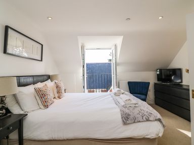 A bedroom with a bed pillows lamps a dresser a chair and an open door leading to a balcony at Castle Cove View in Castle Cove