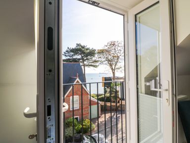 An open balcony door overlooking a street with a brick house trees and the sea beyond at Castle Cove View in Castle Cove