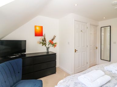A bedroom with a black dresser holding a vase of flowers and a television a blue chair two white doors a full-length mirror and a bed with folded towels at Castle Cove View in Castle Cove