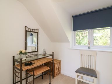 A small room with a wicker vanity table, mirror, chair, and window with a blue roller blind at Castle Cove View in Castle Cove