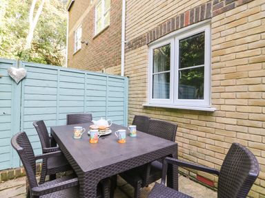 An outdoor patio area with a brown wicker table and six chairs set against a yellow brick wall with a blue wooden fence at Castle Cove View in Castle Cove