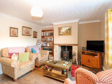 A living room with armchairs a bookshelf a fireplace and a television at Rose Cottage in Downham Market