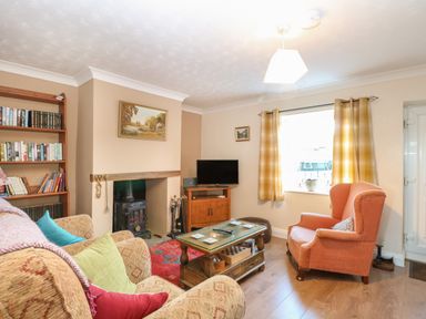 A living room with armchairs a coffee table a wood burning stove and a bookshelf at Rose Cottage in Downham Market