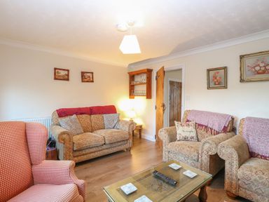 A sitting room with upholstered chairs a glass coffee table wooden floor and framed pictures on the walls at Rose Cottage in Downham Market