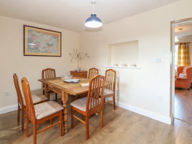 A dining room with a wooden table and six chairs a painting on the wall and teacups on a shelf at Rose Cottage in Downham Market