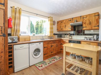 A kitchen with wooden cabinets a window dishwasher washing machine and a rolling kitchen island at Rose Cottage in Downham Market