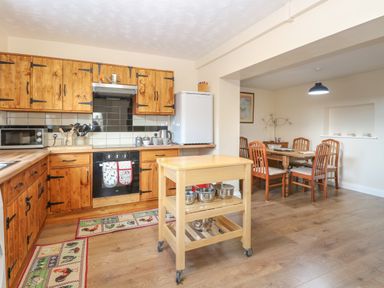 A kitchen with wooden cabinets, a mobile wooden island with pots, and a dining area with a wooden table and chairs at Rose Cottage in Downham Market