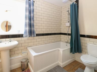 A bathroom with a bathtub shower combination a toilet pedestal sink and window at Rose Cottage in Downham Market