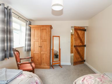 A bedroom with a wooden wardrobe a mirror a chair with orange fabric and a wooden door at Rose Cottage in Downham Market