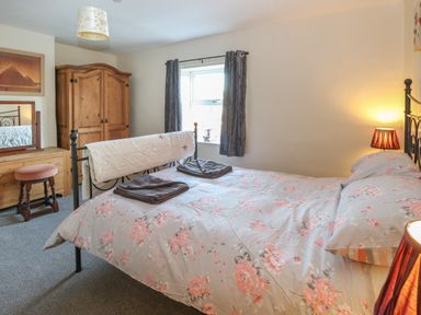 A bedroom with a double bed with floral bedding a wooden wardrobe a dressing table and stool and a window with curtains at Rose Cottage in Downham Market