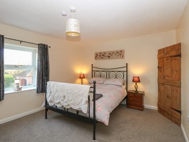 A bedroom with a metal bed frame floral bedding bedside tables with lamps a wooden door and a window at Rose Cottage in Downham Market