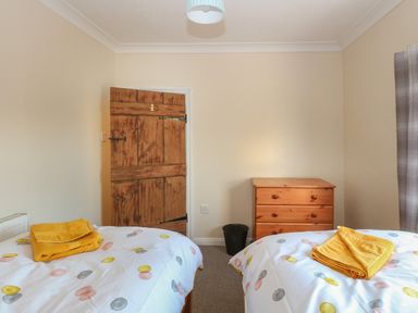 A bedroom with two beds with polka dot bedspreads and yellow towels a wooden door a wooden chest of drawers and a waste bin at Rose Cottage in Downham Market