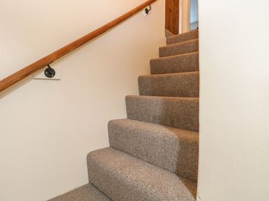 A carpeted staircase with a wooden handrail along a white wall at Rose Cottage in Downham Market