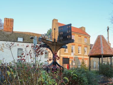 A street scene with a signpost reading Stoke Ferry surrounded by plants and buildings in the background at Rose Cottage in Downham Market